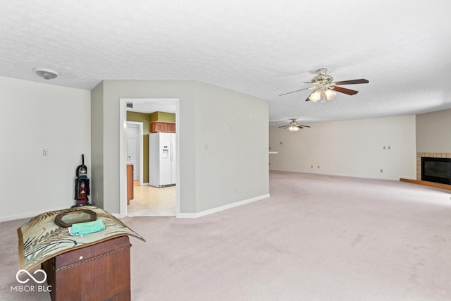 living area featuring a ceiling fan, baseboards, a textured ceiling, a tiled fireplace, and light carpet