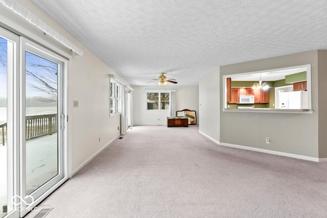 unfurnished living room with ceiling fan with notable chandelier, baseboards, and light carpet