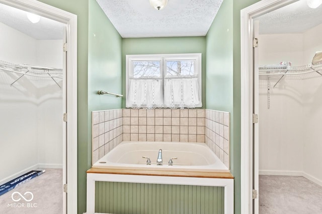 bathroom with a spacious closet, a bath, baseboards, and a textured ceiling