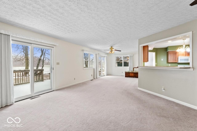 unfurnished living room featuring ceiling fan with notable chandelier, light colored carpet, visible vents, and baseboards