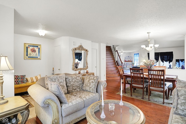 living area featuring stairway, wood finished floors, a textured ceiling, and a chandelier