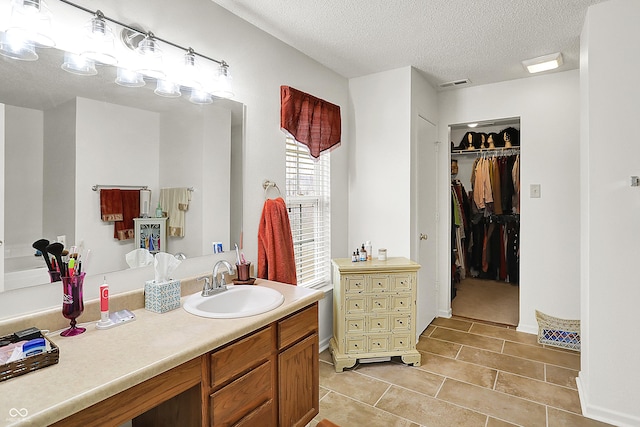 bathroom featuring a spacious closet, visible vents, vanity, tile patterned floors, and a textured ceiling