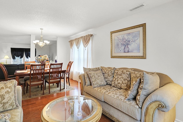 living area featuring a textured ceiling, wood finished floors, visible vents, and a chandelier