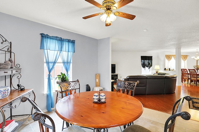 dining room with baseboards, a textured ceiling, light wood-style flooring, and ceiling fan with notable chandelier