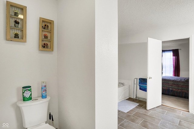 bathroom featuring toilet, a textured ceiling, and a garden tub