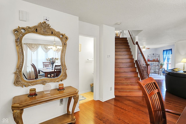 stairs with an inviting chandelier, wood finished floors, baseboards, and a textured ceiling