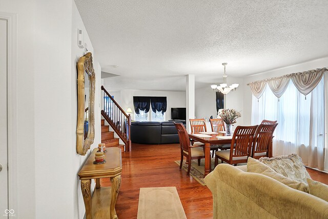 dining space featuring stairway, a notable chandelier, wood finished floors, and a textured ceiling