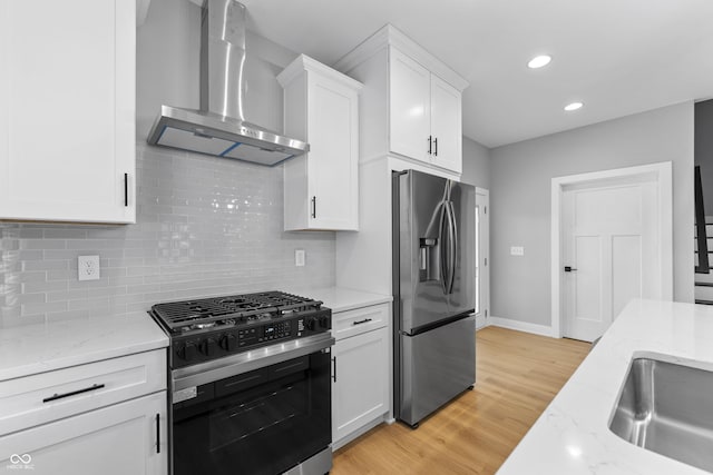 kitchen with light wood finished floors, tasteful backsplash, appliances with stainless steel finishes, white cabinetry, and wall chimney range hood