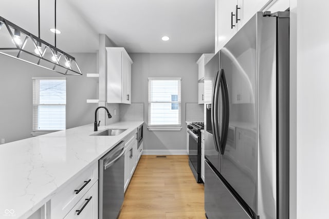 kitchen with a sink, light wood-style floors, white cabinets, appliances with stainless steel finishes, and backsplash