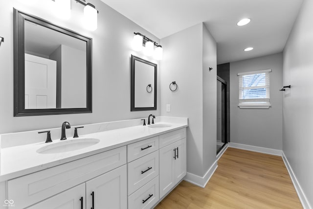 full bath with double vanity, wood finished floors, a sink, and baseboards