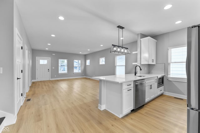 kitchen featuring light countertops, appliances with stainless steel finishes, white cabinets, a sink, and light wood-type flooring