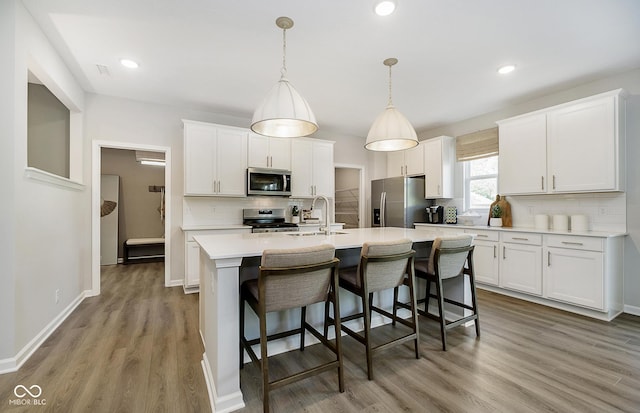 kitchen with wood finished floors, white cabinetry, light countertops, appliances with stainless steel finishes, and an island with sink