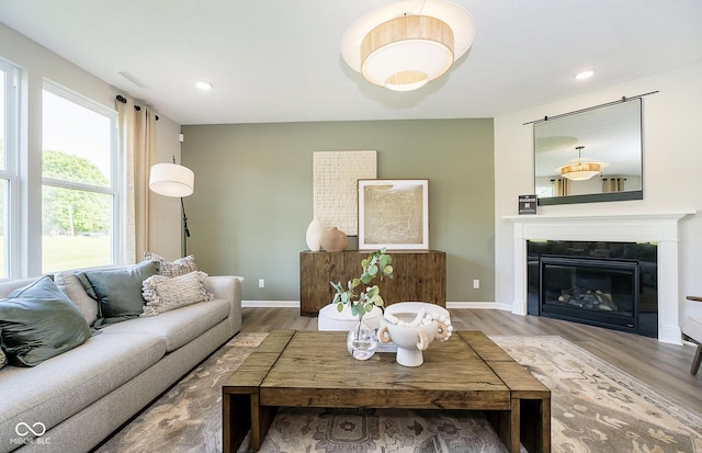 living area featuring a glass covered fireplace, recessed lighting, baseboards, and wood finished floors