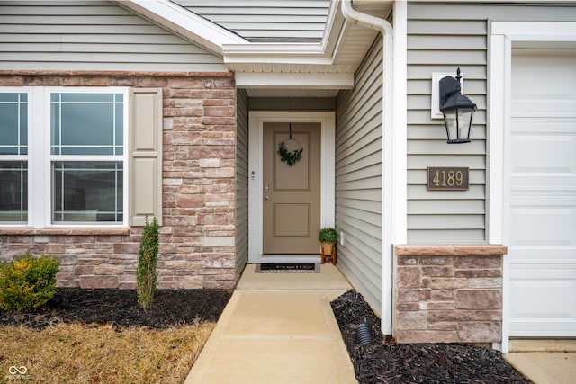 entrance to property featuring a garage, stone siding, and brick siding