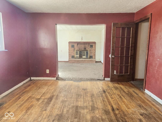 unfurnished room featuring a textured ceiling, a fireplace, hardwood / wood-style flooring, and baseboards