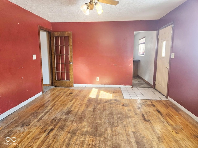 empty room with a ceiling fan, baseboards, a textured ceiling, and hardwood / wood-style floors