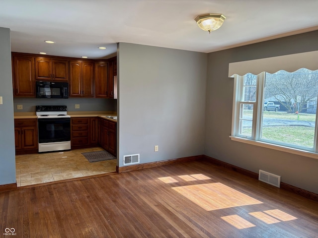 kitchen featuring light wood-type flooring, visible vents, black microwave, and range with electric cooktop