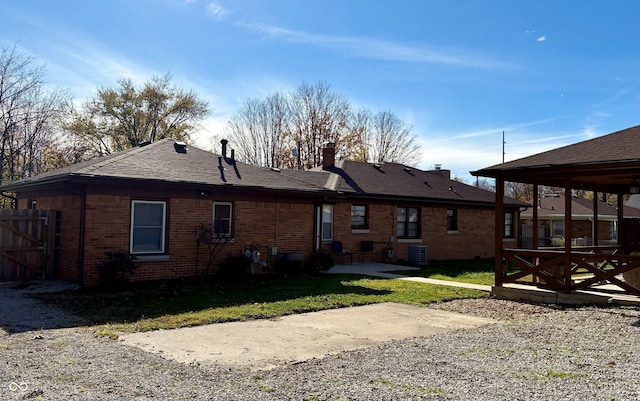 back of house with brick siding, a shingled roof, a lawn, a chimney, and a patio area