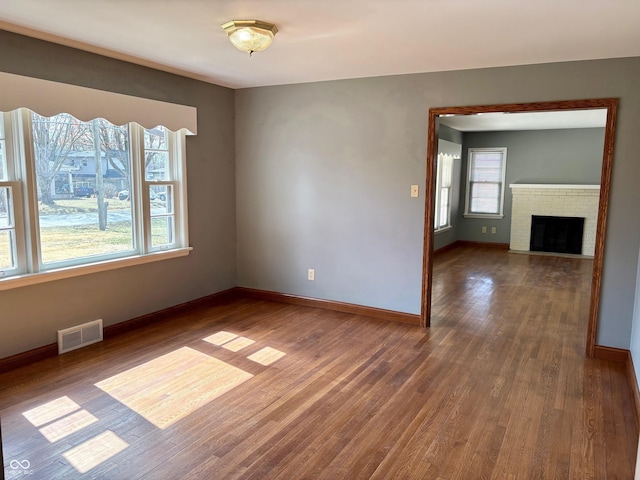 unfurnished room featuring wood finished floors, a healthy amount of sunlight, visible vents, and baseboards