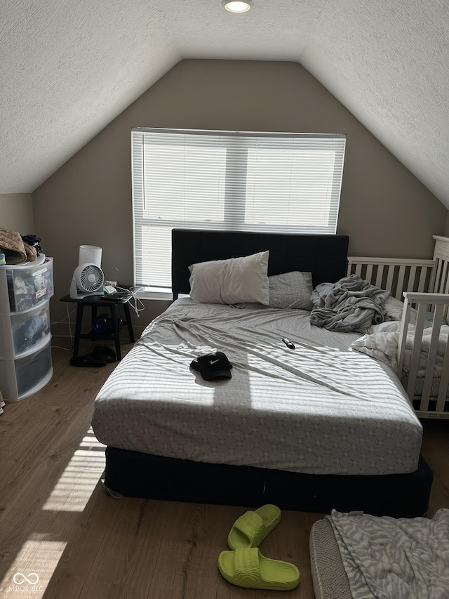 bedroom with vaulted ceiling, multiple windows, wood finished floors, and a textured ceiling