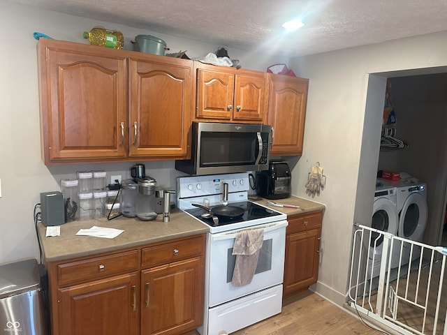 kitchen with washer and clothes dryer, white electric range, stainless steel microwave, a textured ceiling, and brown cabinetry