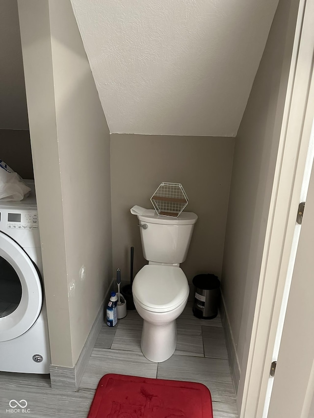 bathroom featuring a textured ceiling, toilet, washer / dryer, and vaulted ceiling