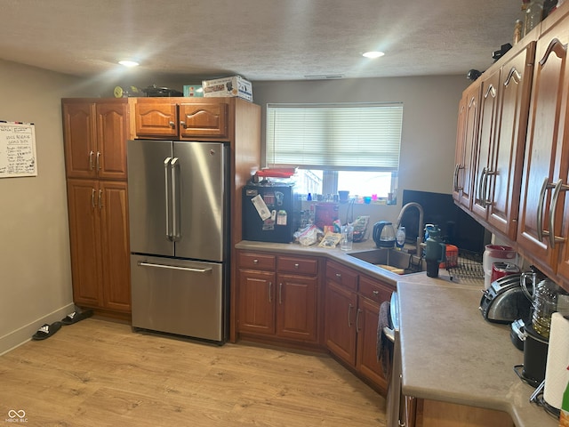 kitchen with brown cabinets, a sink, freestanding refrigerator, light wood-style floors, and light countertops