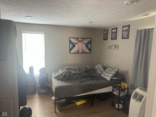 bedroom featuring visible vents, a textured ceiling, and wood finished floors