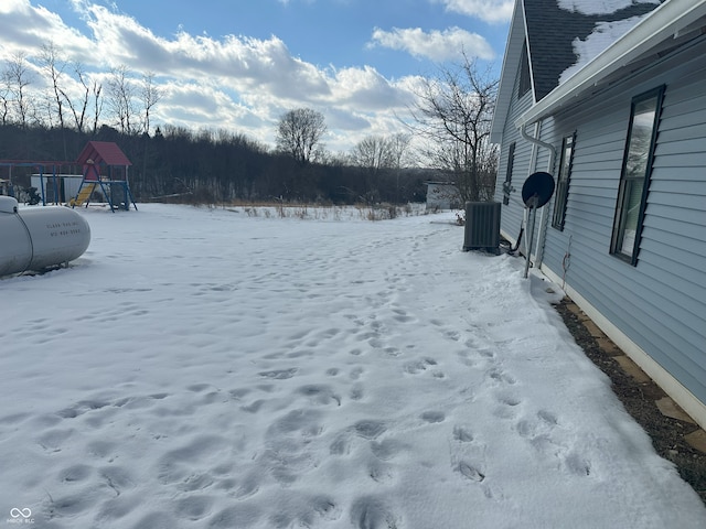 yard covered in snow featuring central AC unit and a playground