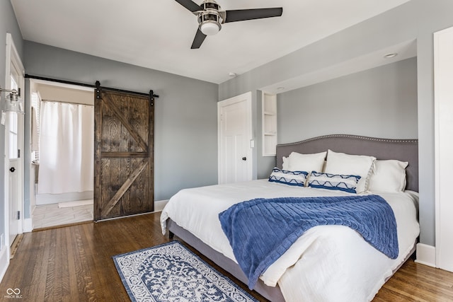 bedroom with ceiling fan, a barn door, and wood finished floors