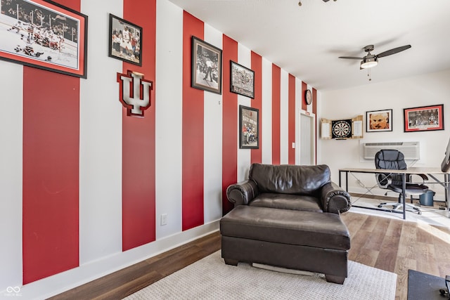 sitting room with baseboards, wood finished floors, a ceiling fan, and a wall unit AC