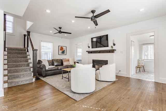 living area featuring stairway, a brick fireplace, a healthy amount of sunlight, and hardwood / wood-style floors