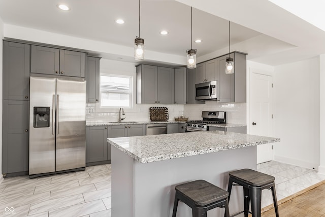 kitchen with light stone counters, gray cabinets, stainless steel appliances, and a sink