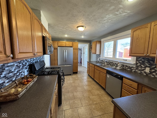 kitchen with appliances with stainless steel finishes, dark countertops, a sink, and decorative backsplash