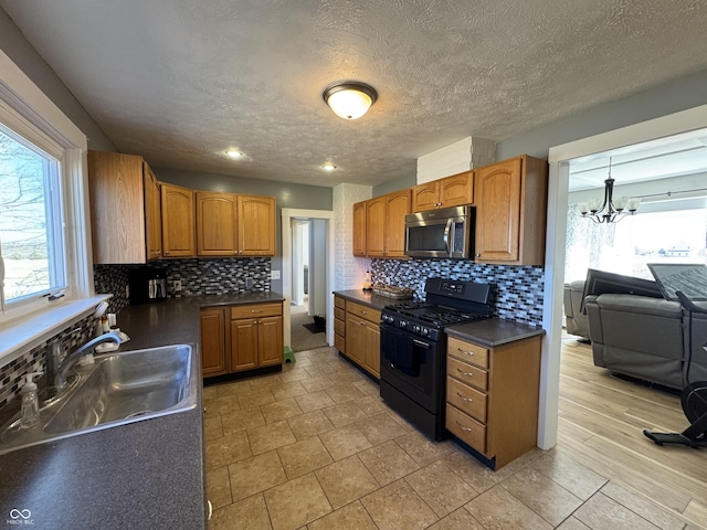 kitchen featuring brown cabinetry, dark countertops, stainless steel microwave, black gas stove, and a sink