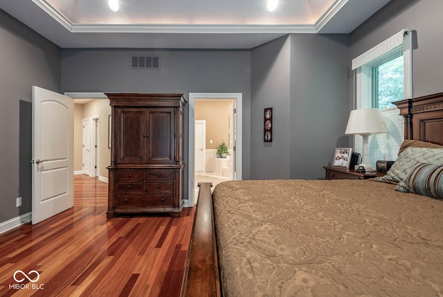 bedroom featuring wood finished floors, baseboards, visible vents, ornamental molding, and a raised ceiling