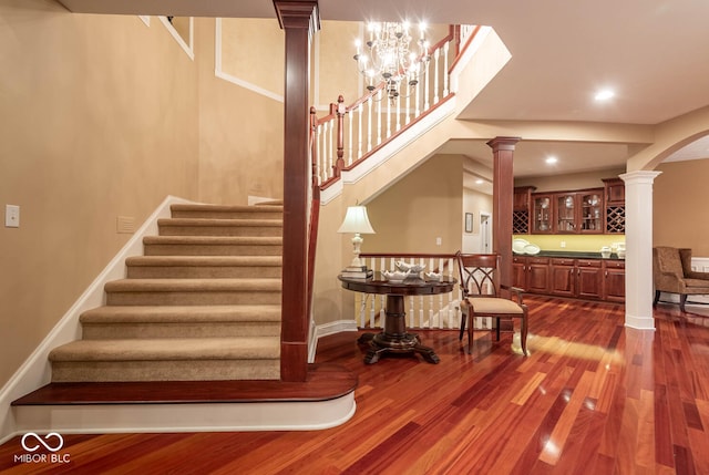 stairway with wood finished floors, recessed lighting, arched walkways, baseboards, and ornate columns