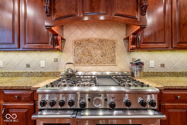 kitchen with stainless steel stove, light stone counters, dark brown cabinets, and backsplash