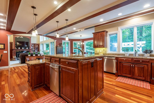 kitchen featuring beamed ceiling, an island with sink, a sink, stainless steel dishwasher, and a fireplace