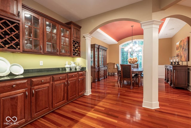 bar featuring a wainscoted wall, wood finished floors, lofted ceiling, a chandelier, and ornate columns