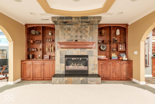 unfurnished living room with a tiled fireplace, crown molding, and built in features