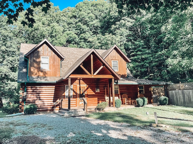 log home with a porch, fence, and a shingled roof