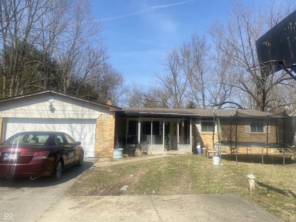 ranch-style home featuring aphalt driveway, a trampoline, an attached garage, a front yard, and brick siding