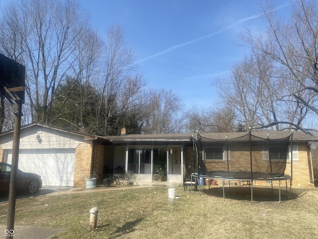 single story home featuring an attached garage, a shingled roof, a front lawn, a trampoline, and brick siding