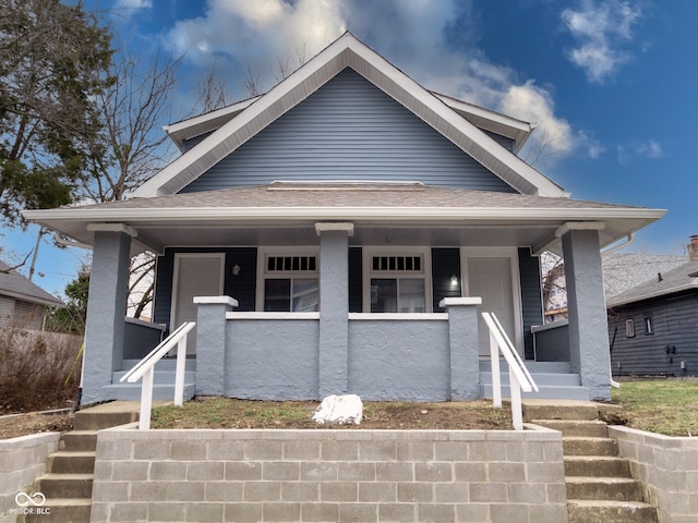 bungalow-style house featuring stucco siding, roof with shingles, and covered porch