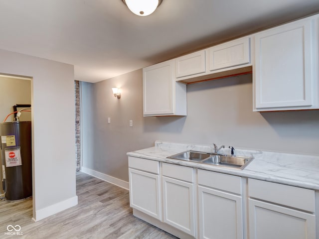 kitchen featuring light wood finished floors, electric water heater, baseboards, white cabinets, and a sink