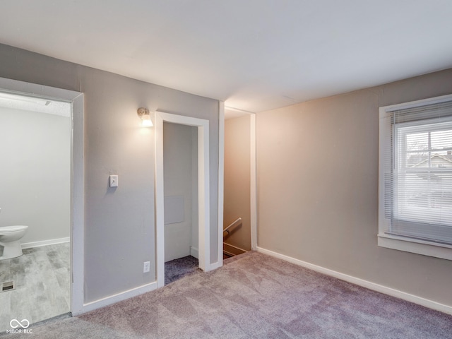 unfurnished bedroom featuring baseboards, ensuite bathroom, and carpet flooring