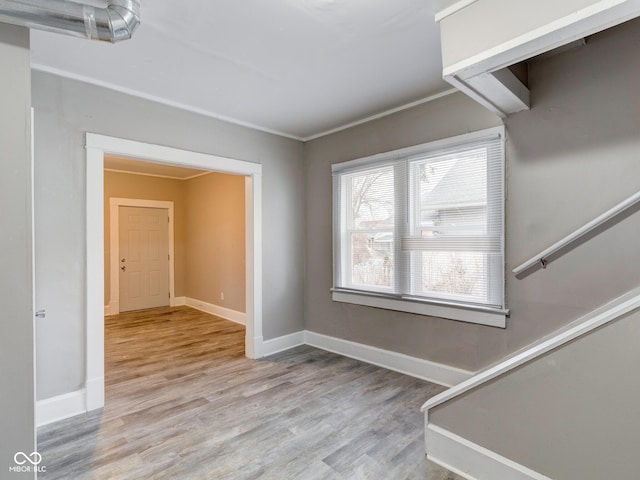 empty room featuring stairs, crown molding, wood finished floors, and baseboards