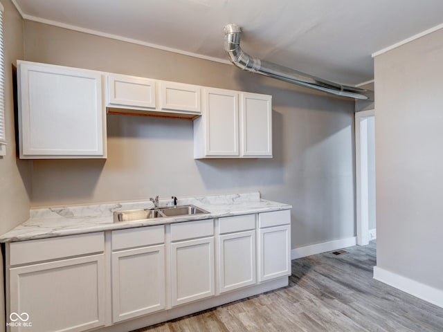 kitchen with light wood-style flooring, ornamental molding, a sink, white cabinetry, and baseboards