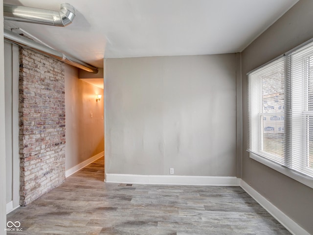 unfurnished room featuring baseboards, wood finished floors, and brick wall